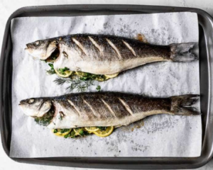 two fish on a baking pan with lemons inside them